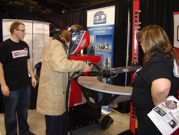 A student wearing a welding facemask that functions as a virtual reality training simulator while holding a training arc welder.