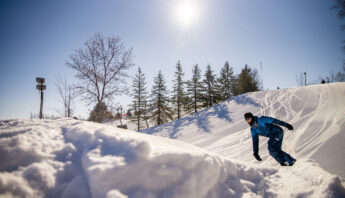 A snowboarder approaches a snowy jump on a ski slope.